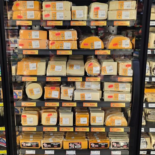 Refrigerated case stocked with blocks and wedges of cheese in a store